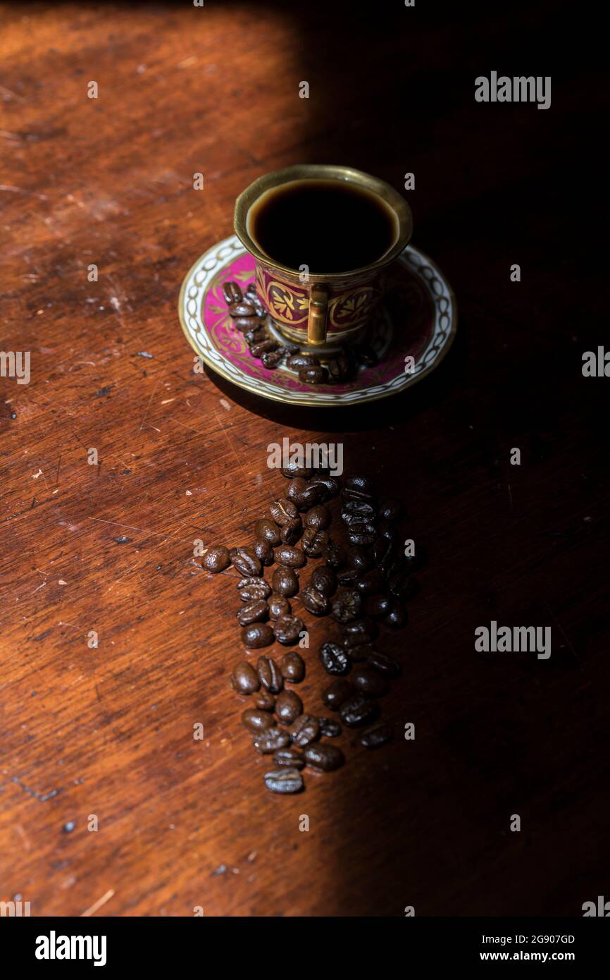 Tazza di caffè e chicchi di caffè crudo giacenti su un tavolo ombreggiato Foto Stock