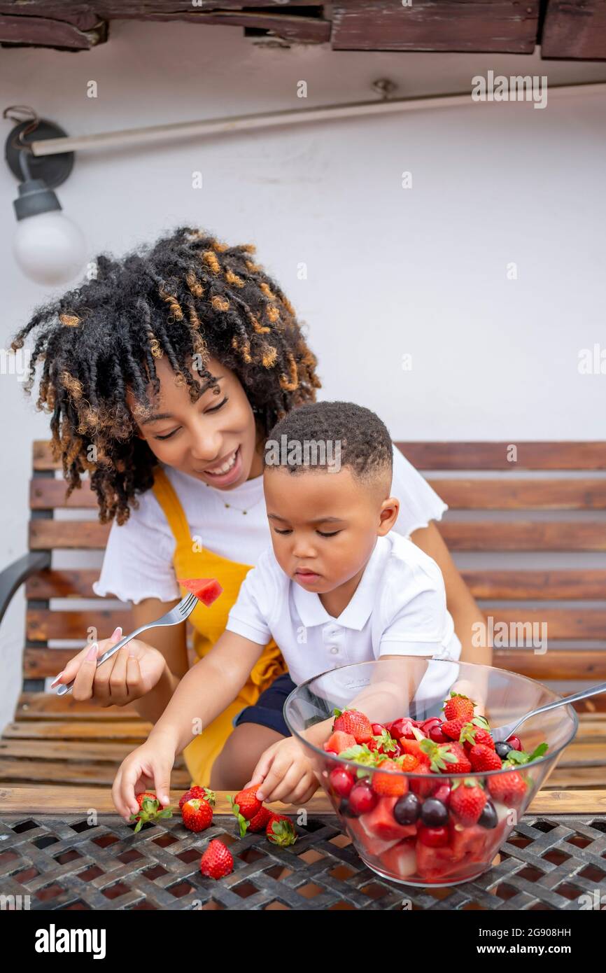 Madre e figlio mangiano Macedonia di frutta mentre si siedono sulla panca Foto Stock