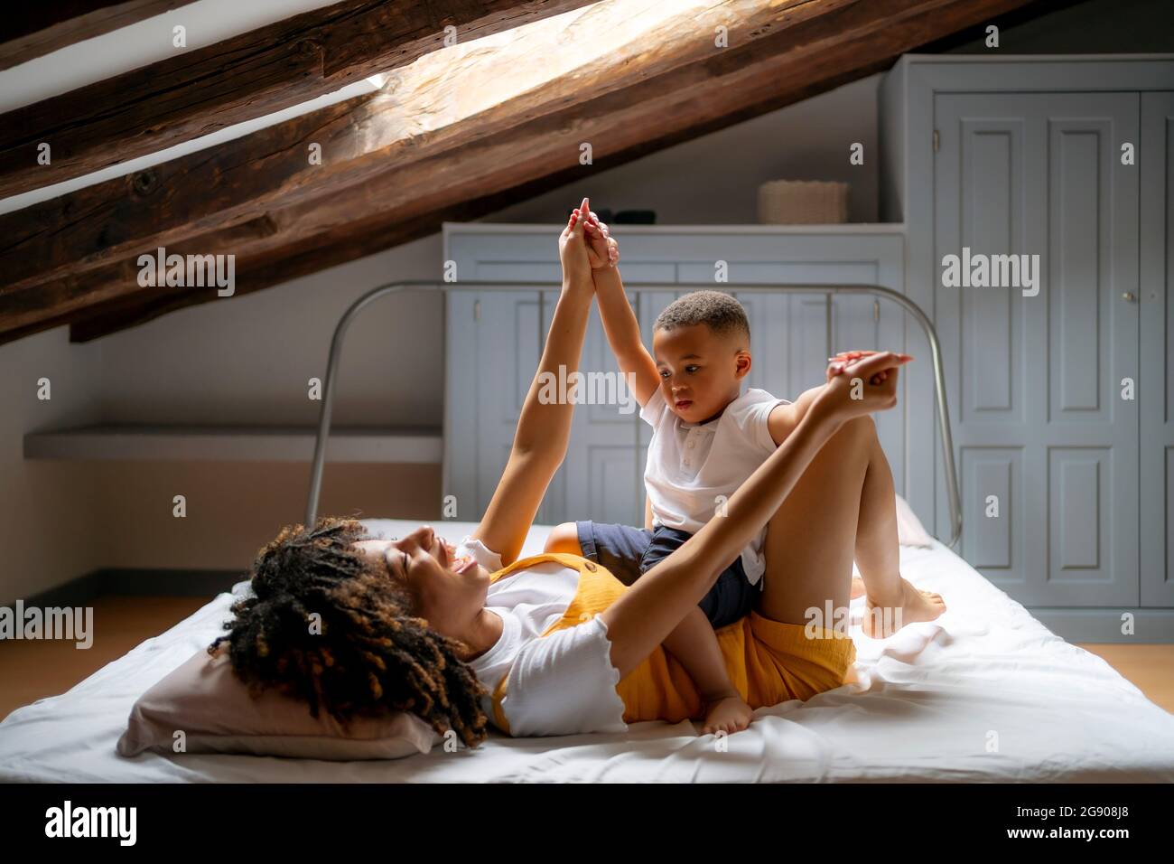 Felice madre che gioca con il figlio mentre si trova a letto in soffitta a casa Foto Stock