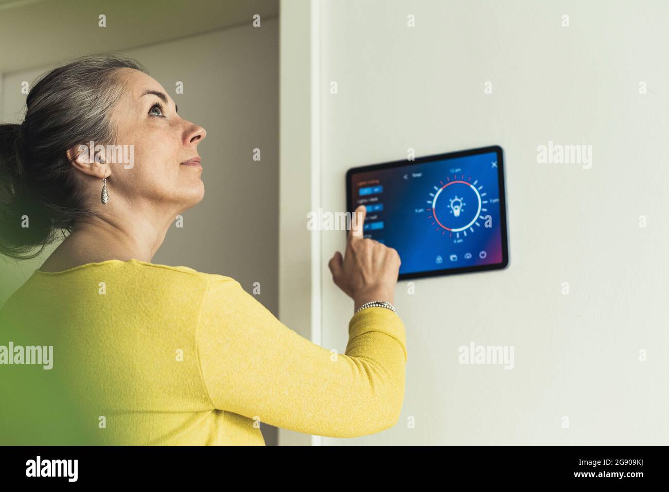 Donna che guarda lontano mentre si trova accanto a un dispositivo di automazione a parete Foto Stock