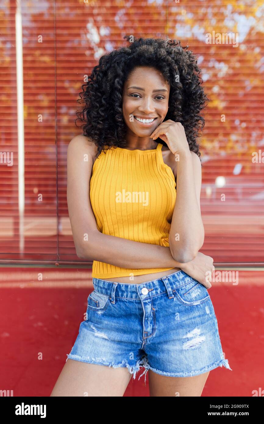 Sorridente giovane donna in piedi di fronte alla finestra rossa Foto Stock