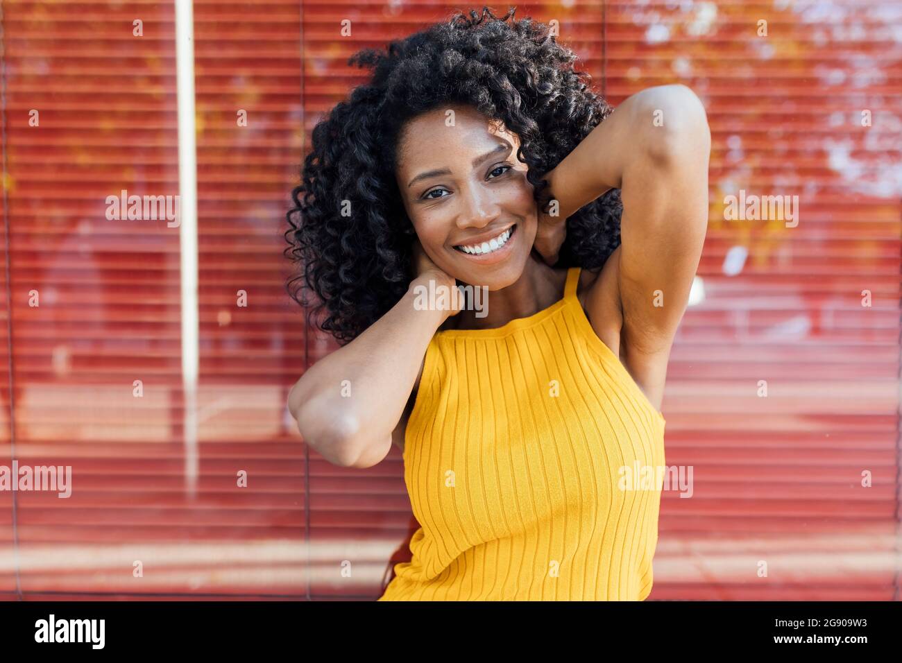 Giovane donna felice con capelli ricci in piedi davanti alla finestra rossa Foto Stock