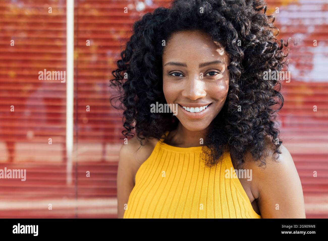 Bella donna sorridente con capelli ricci di fronte alla finestra rossa Foto Stock