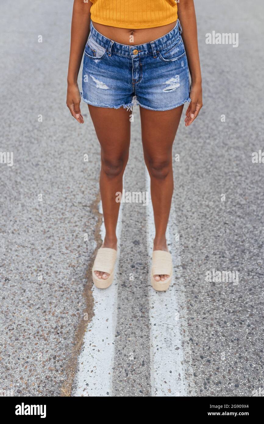 Giovane donna che indossa pantaloncini in denim in piedi su strada Foto Stock