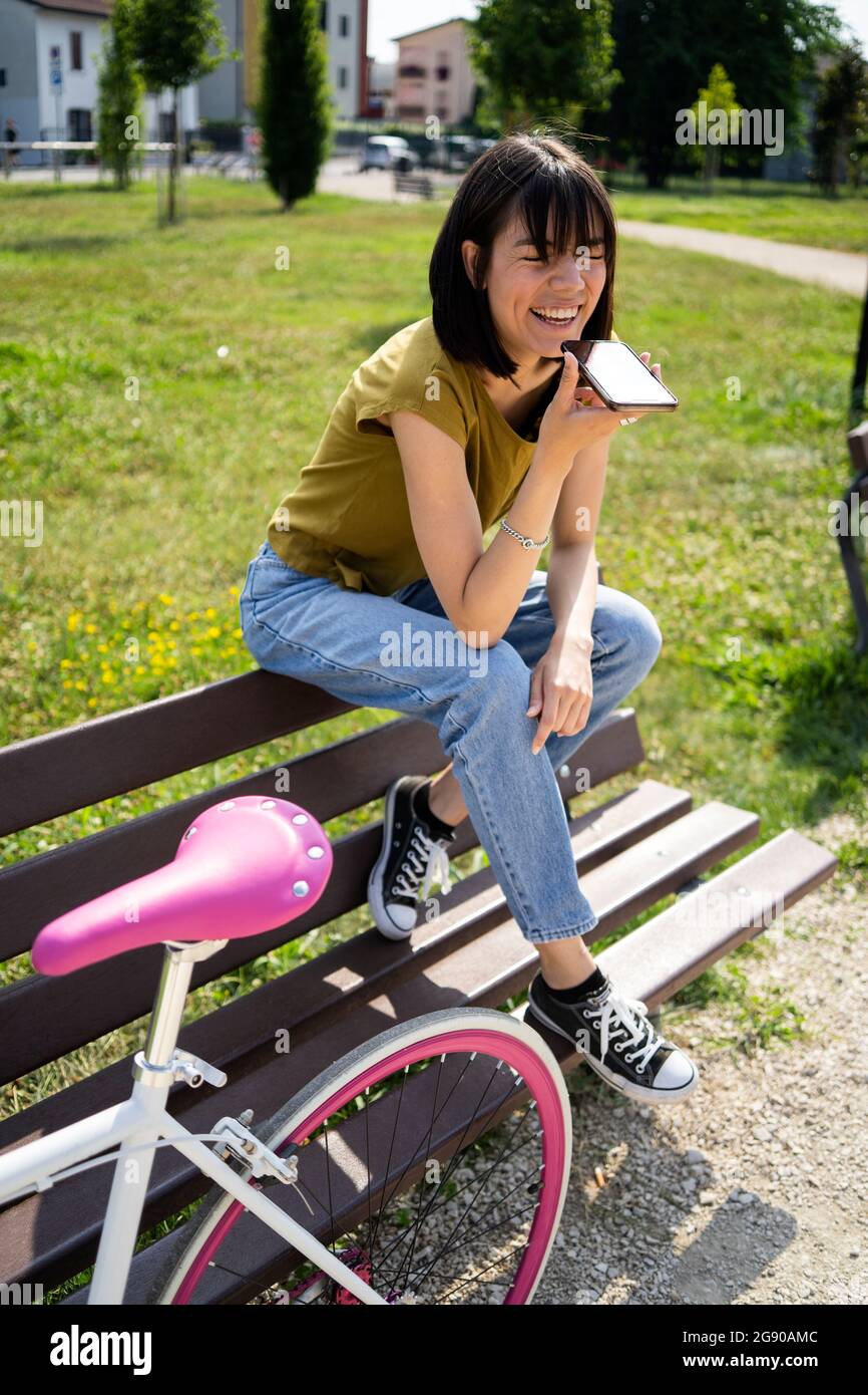 Donna che invia messaggi vocali tramite smartphone mentre è seduto sul banco Foto Stock