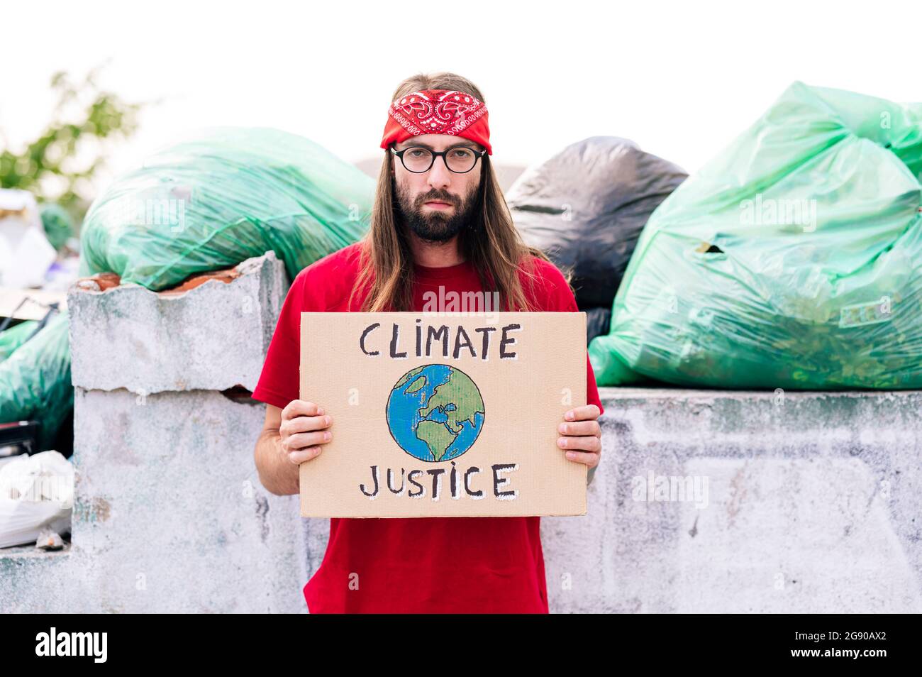 Hippie uomo che tiene clima giustizia cartone vicino spazzatura dump Foto Stock