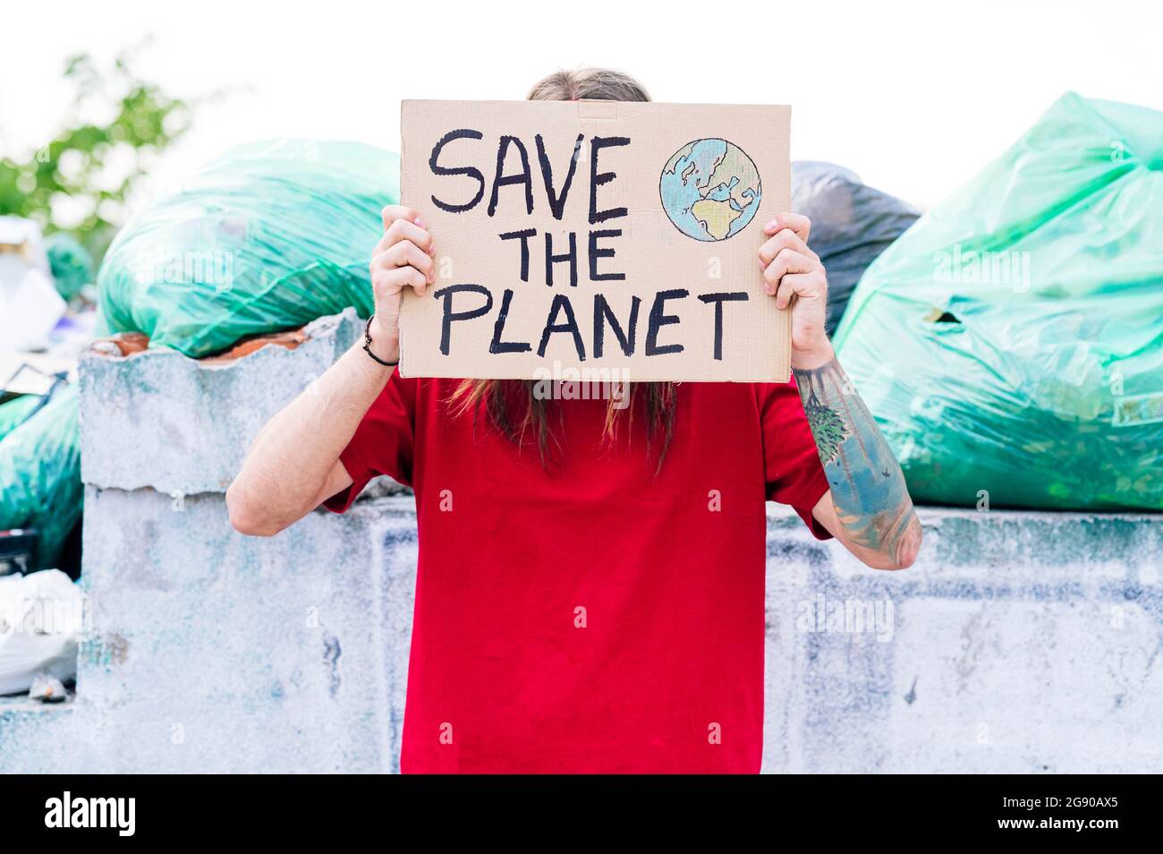 Hippie uomo che copre faccia con salvare il cartone pianeta vicino spazzatura dump Foto Stock