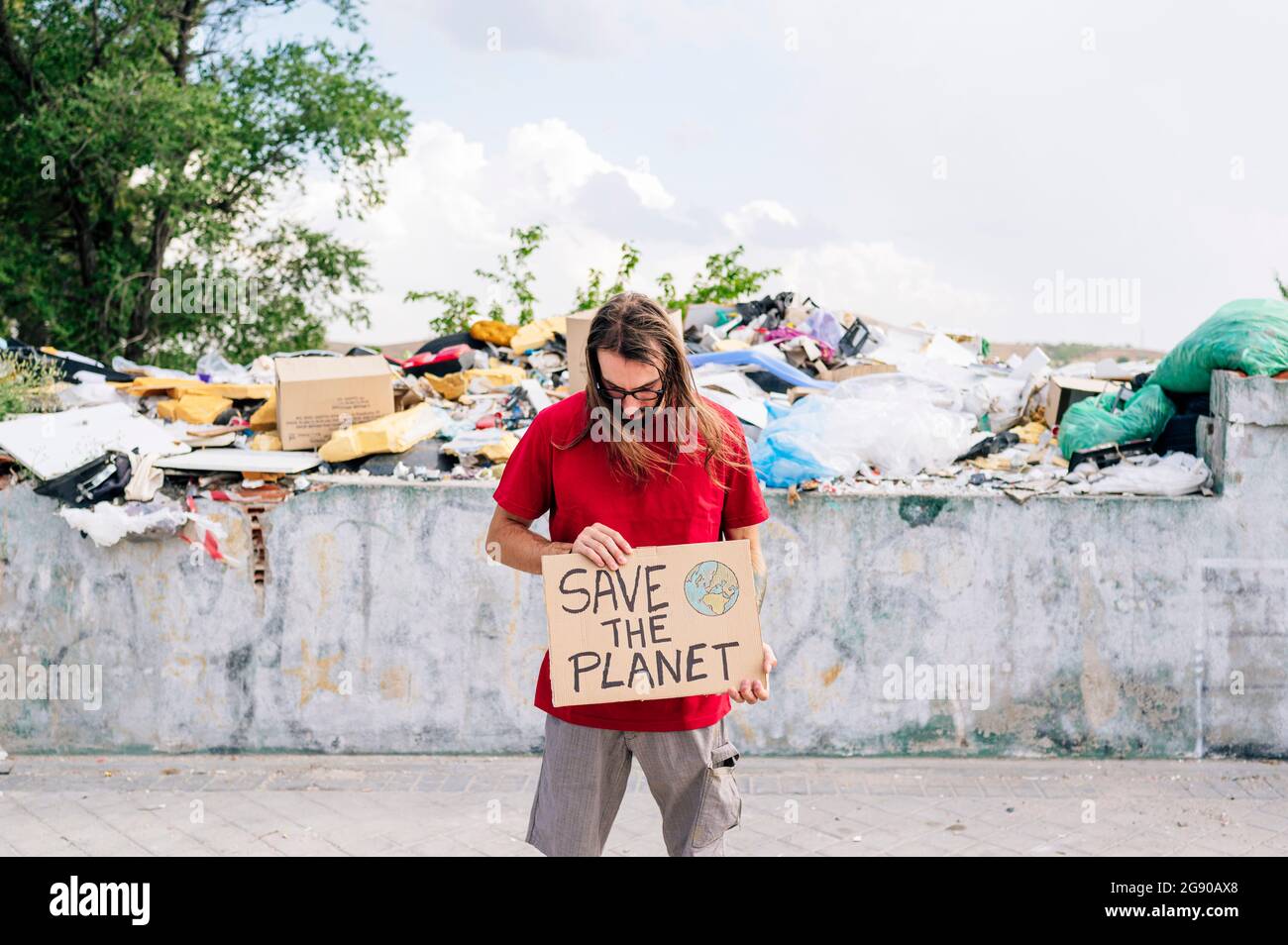 Uomo che tiene salvare il cartone pianeta di fronte a spazzatura dump Foto Stock