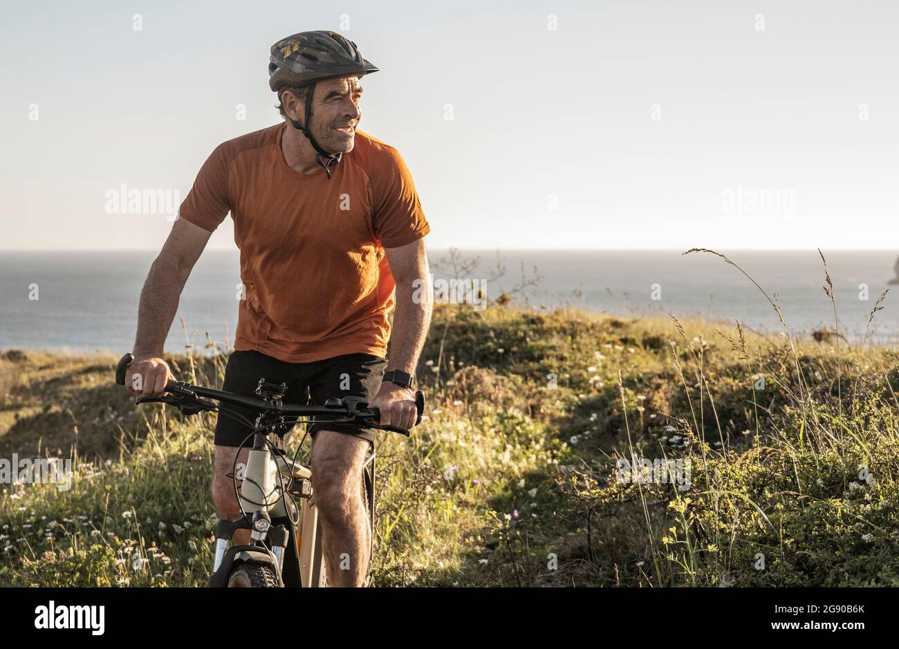 Atleta maschile in bicicletta guardando lontano al tramonto Foto Stock