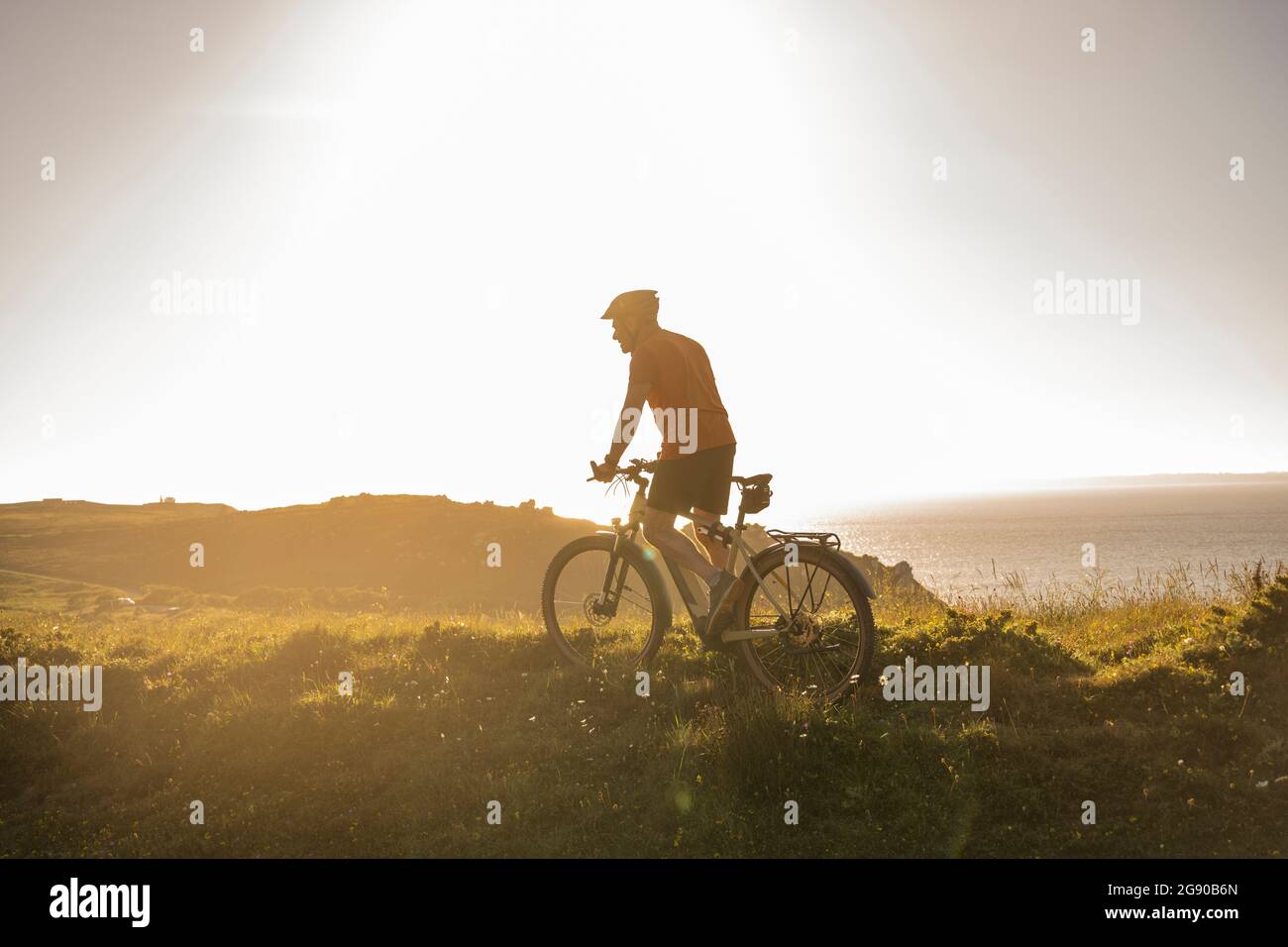 Atleta maschile maturo che guida in mountain bike al tramonto Foto Stock