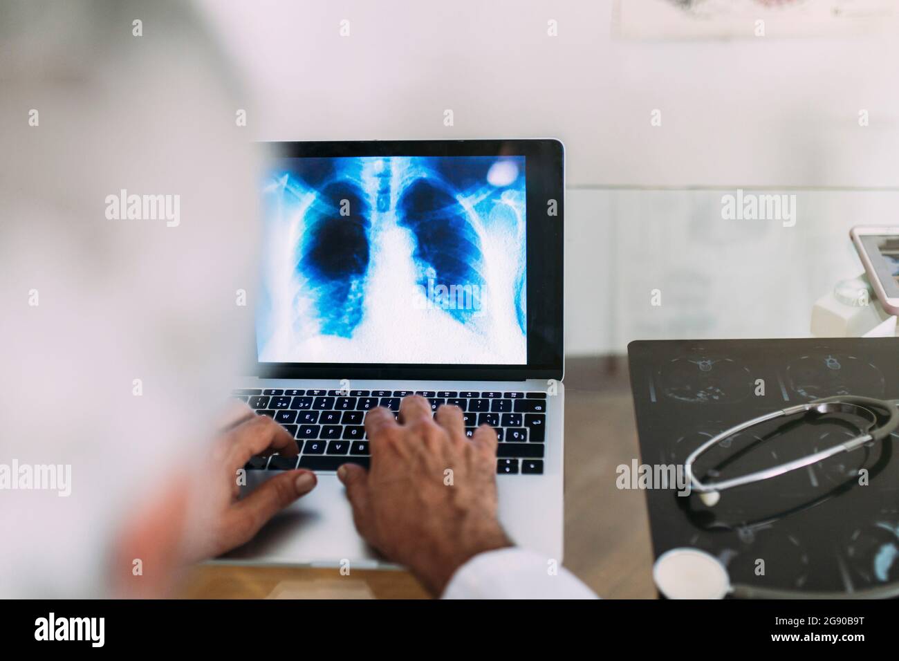 Medico di sesso maschile che usa il computer portatile mentre lavora a raggi X in clinica Foto Stock