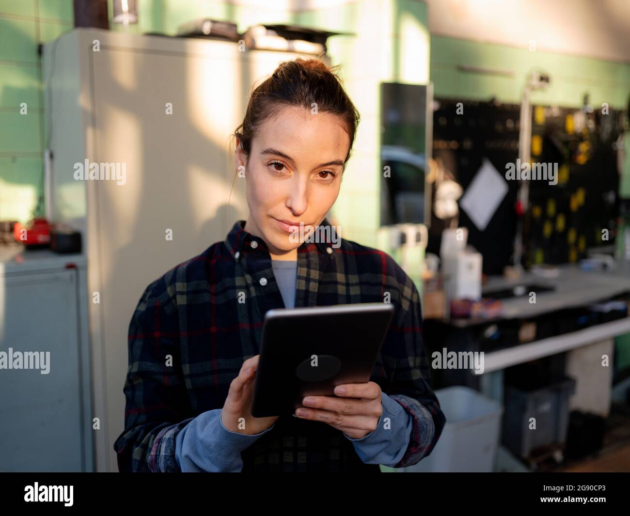 Meccanico femminile con tablet digitale in piedi presso il negozio di riparazione auto Foto Stock