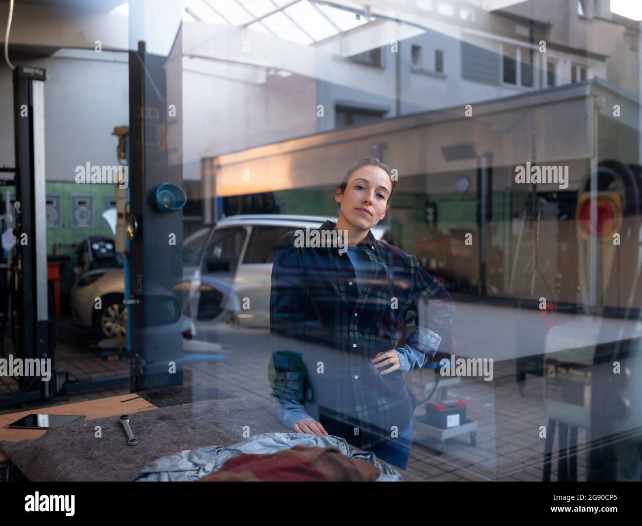 Meccanico femminile in piedi presso il negozio di riparazione auto visto attraverso la finestra Foto Stock