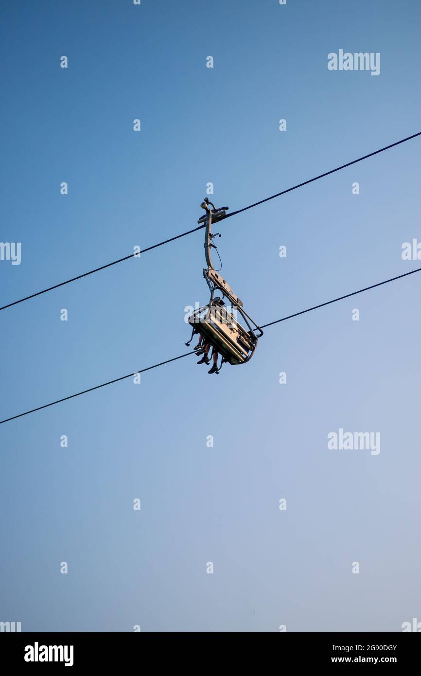 Seggiovia a quattro posti con un paio di turisti mentre lo si usa visto dal basso contro il cielo blu. Foto Stock