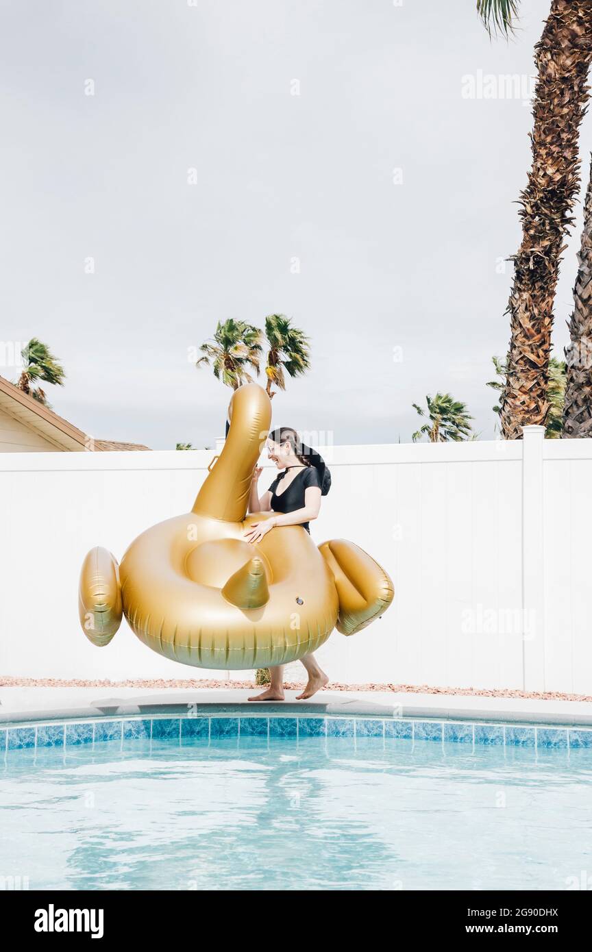 Donna con cigno gonfiabile che cammina a bordo piscina durante la vacanza Foto Stock