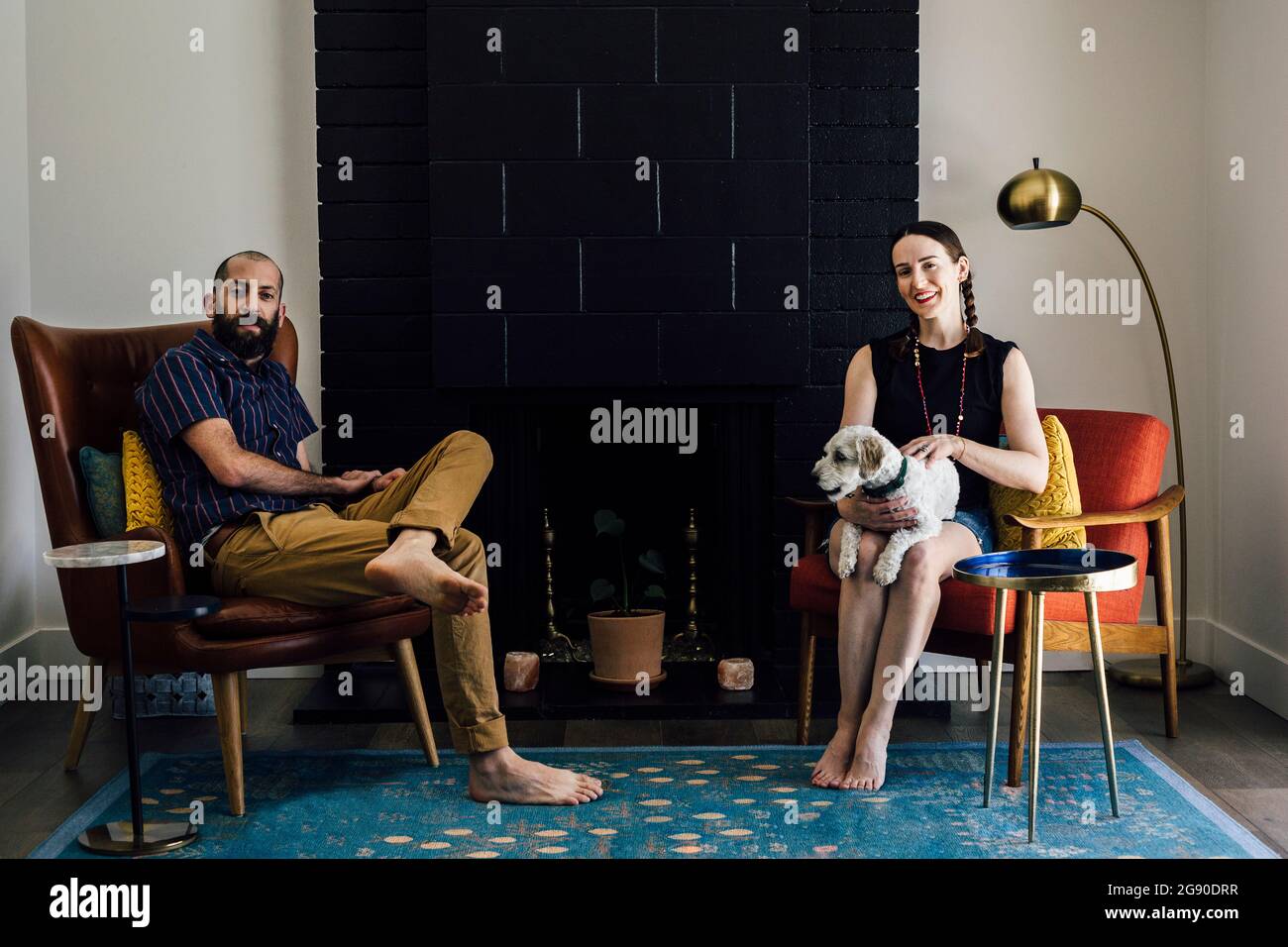 Donna sorridente con cane seduto in grembo davanti all'uomo in soggiorno Foto Stock
