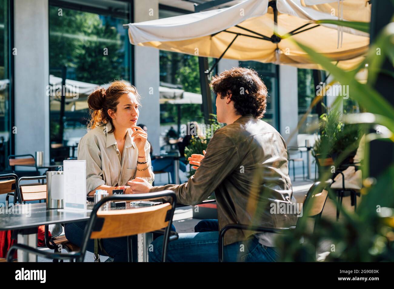 La coppia parla mentre sii al caffè sul marciapiede durante la giornata di sole Foto Stock