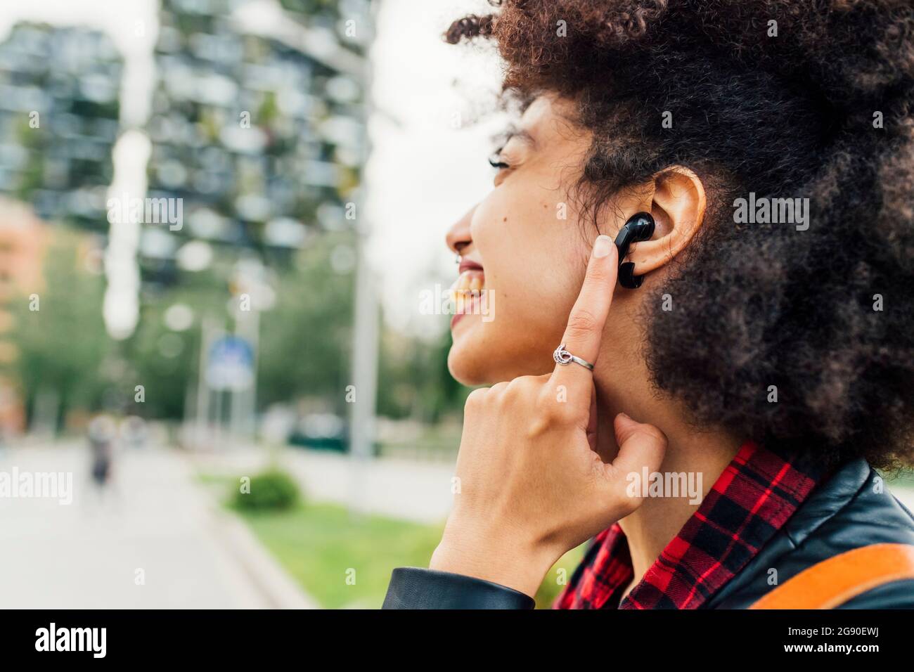Allegra giovane donna che tocca le cuffie intrauricolari wireless Foto Stock