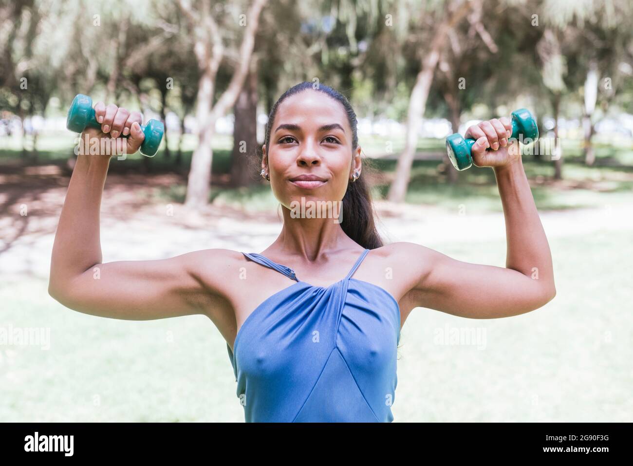 Atleta femminile con pesi a mano che praticano al parco pubblico Foto Stock