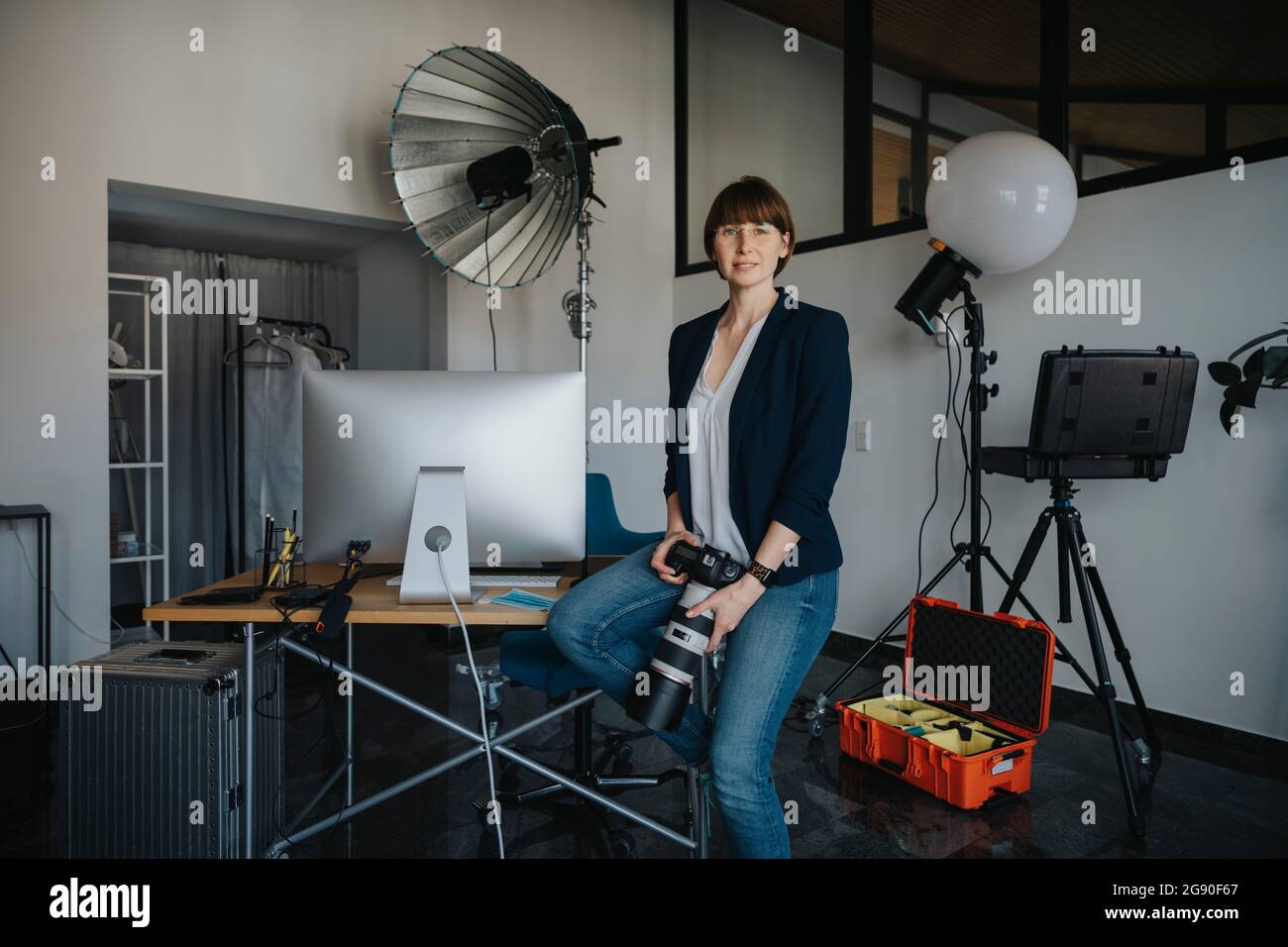 Fotografa fidata e dotata di fotocamera digitale mentre si siede sulla scrivania dello studio Foto Stock