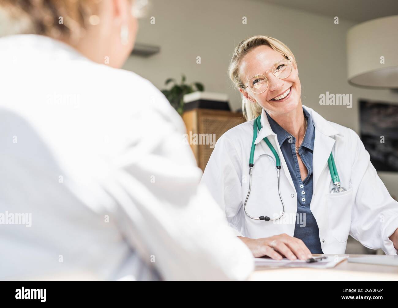 Medico femminile sorridente mentre guarda il paziente in ufficio Foto Stock