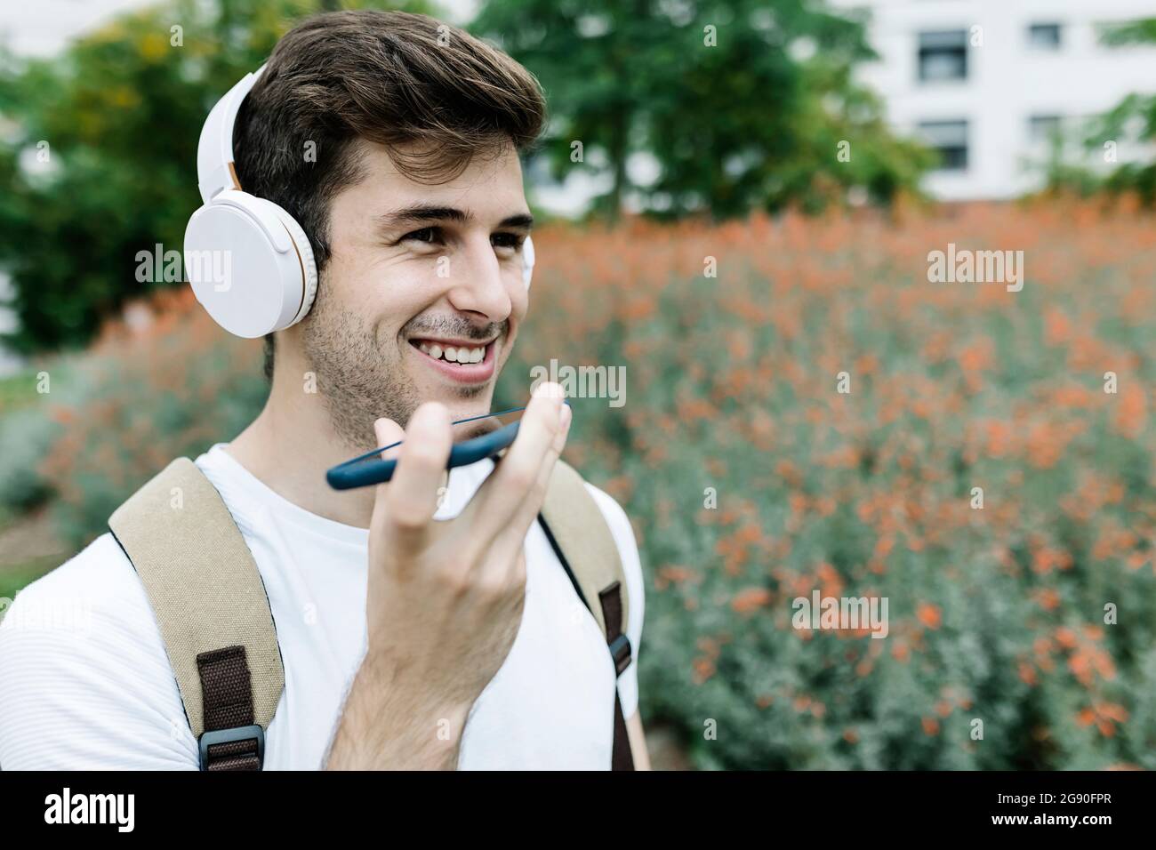 Sorridente giovane che invia la segreteria telefonica tramite telefono cellulare da prato Foto Stock