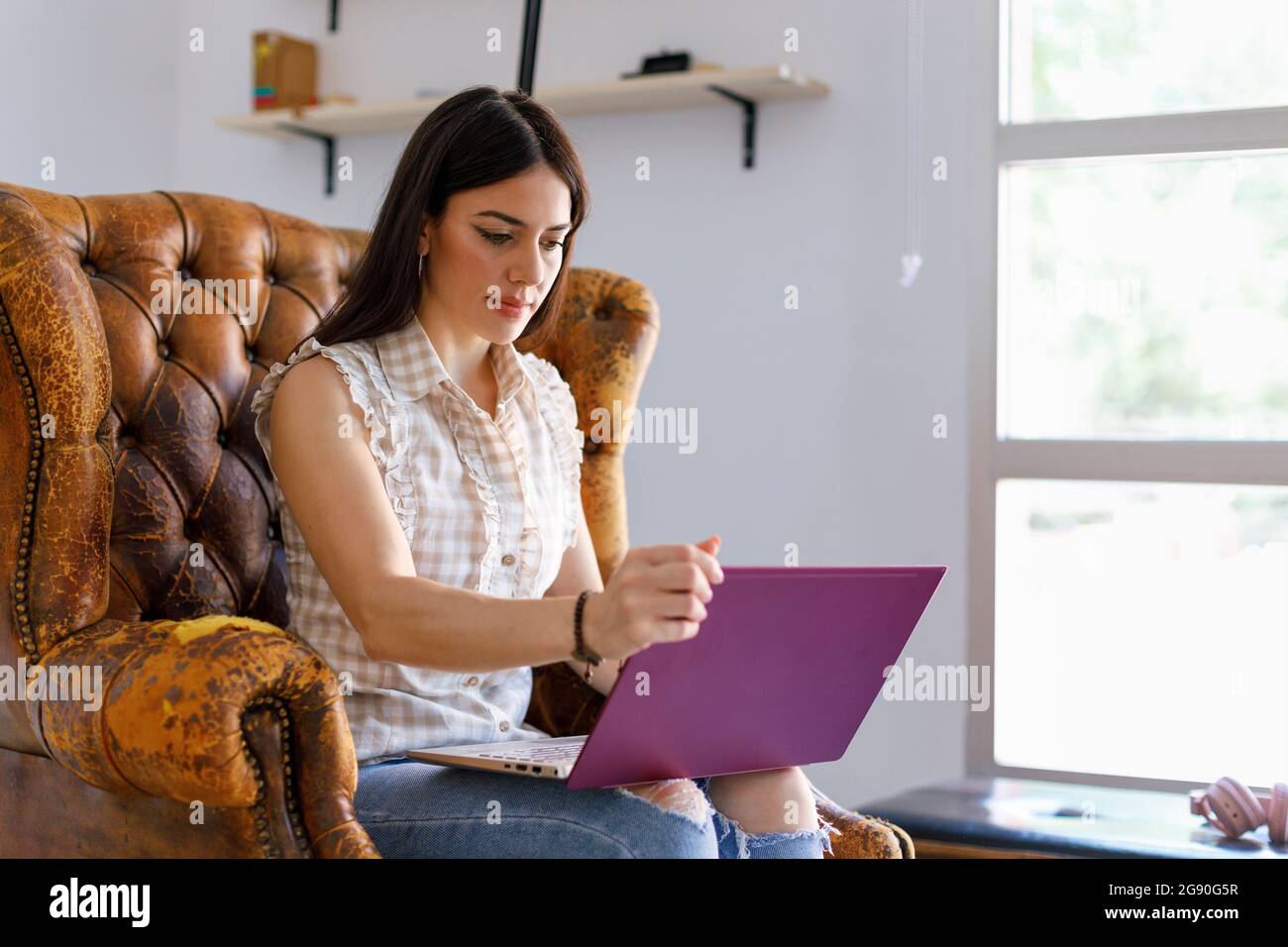 Donna creativa professionale che tiene il laptop mentre si siede sulla poltrona in studio Foto Stock