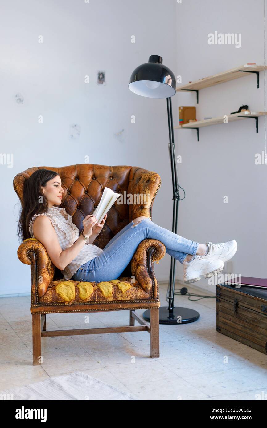Donna lettura libro mentre seduto su poltrona in studio dell'artista Foto Stock