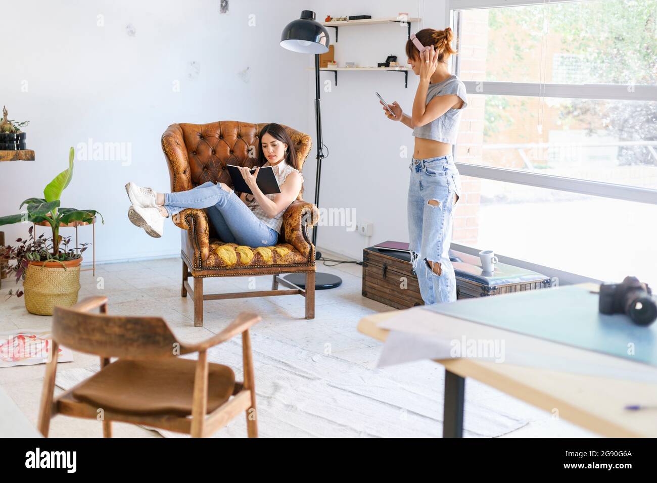 Giovane fotografo femminile che ascolta musica mentre un collega legge un libro in studio Foto Stock