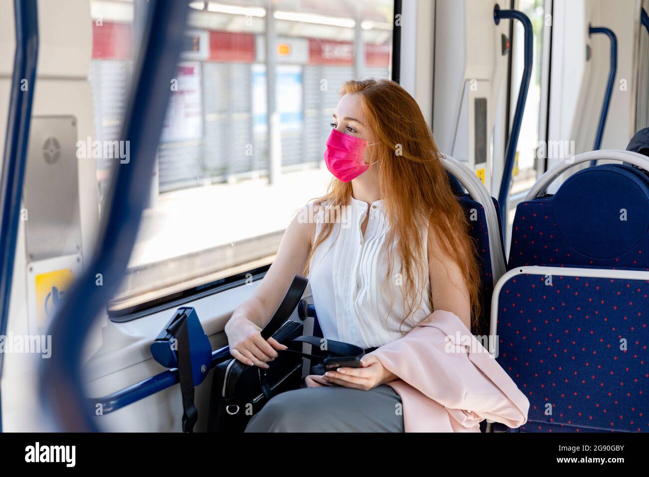 Donna d'affari in maschera protettiva che guarda attraverso la finestra mentre si passa in treno Foto Stock