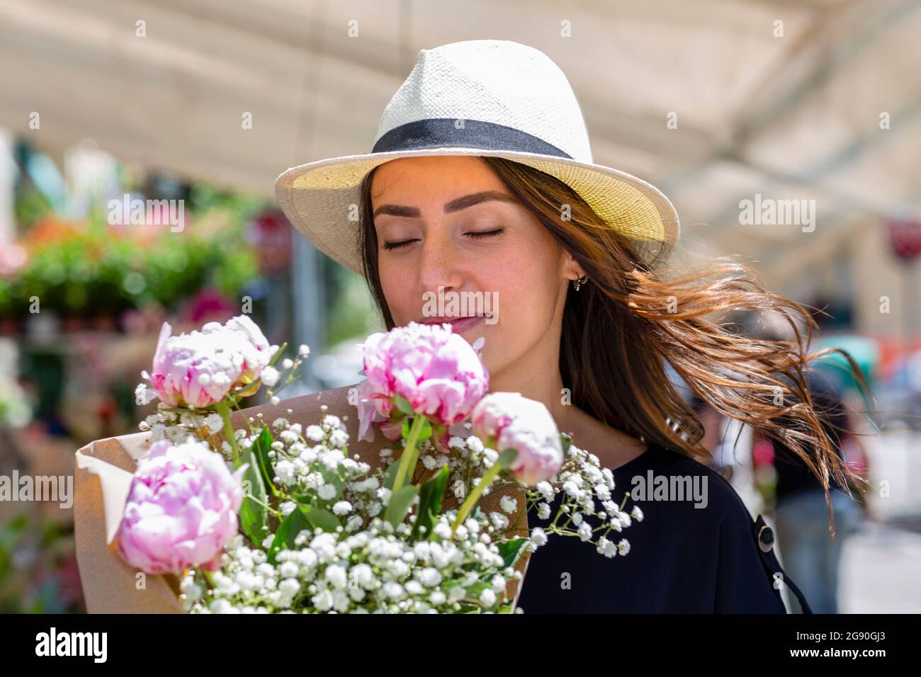 Donna in cappello di sole che odora peonie fiore bouquet vicino negozio di fiori Foto Stock