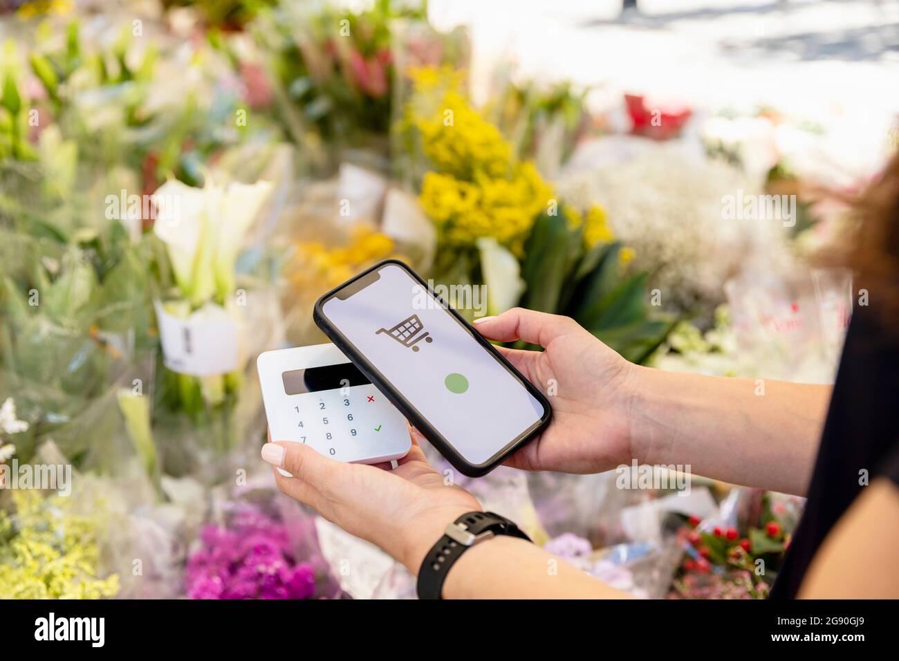 Donna che tiene lo smartphone mentre fa il pagamento contactless al negozio di fiori Foto Stock