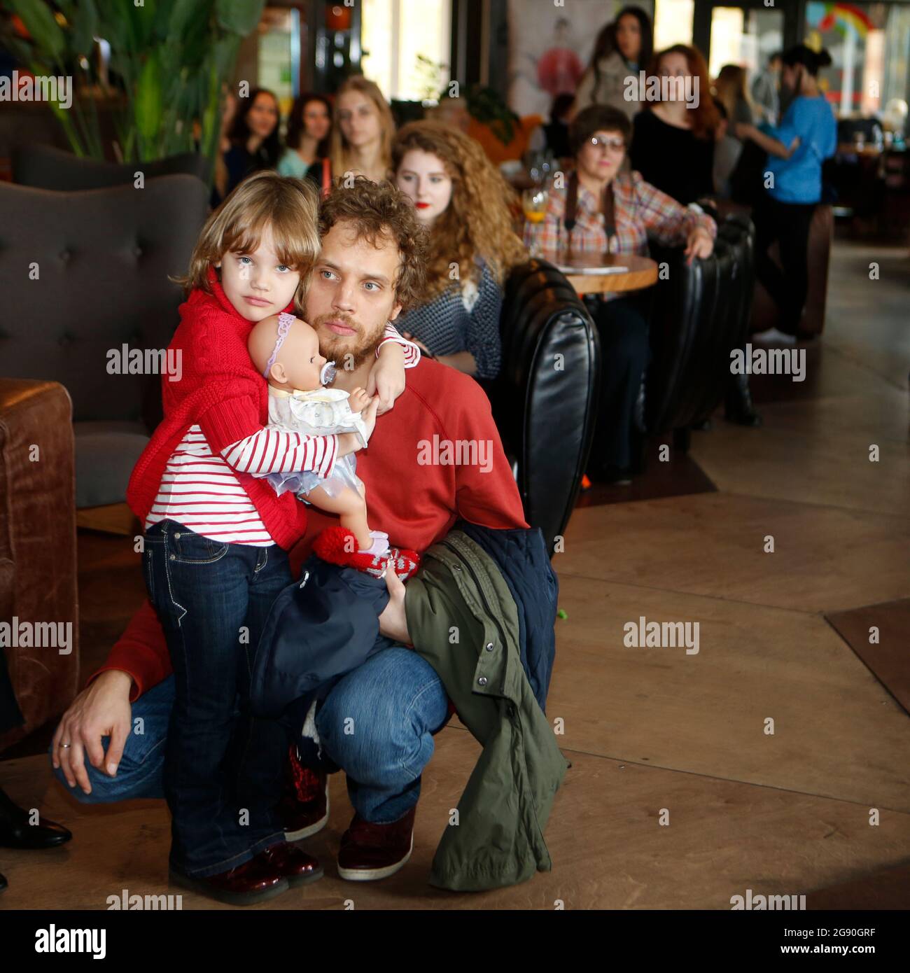 Bella Natalia Vodianova look-like bambina in pullover rosso e jeans + giocattolo in mani fotografato con suo padre alla presentazione di moda a Kiev Foto Stock