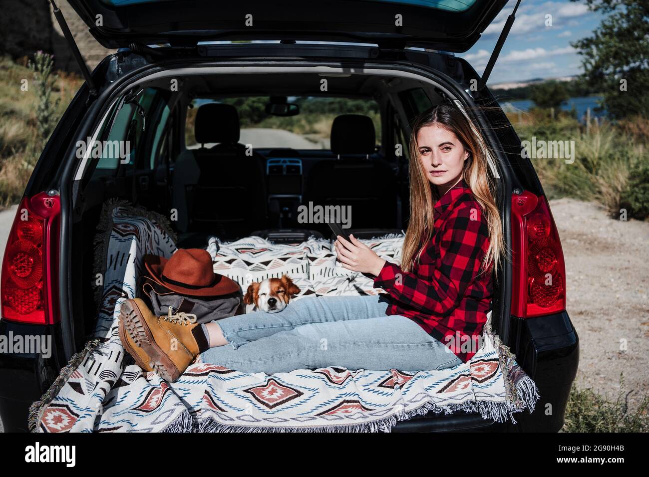 Bella giovane donna che guarda via mentre si siede con il cane nel bagagliaio auto il giorno di sole Foto Stock
