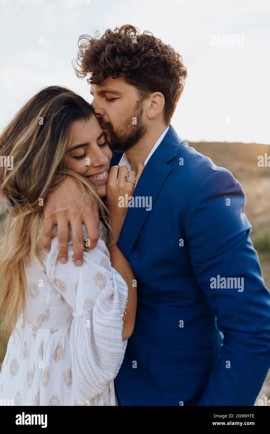 Uomo con braccio intorno baciare la ragazza al tramonto Foto Stock