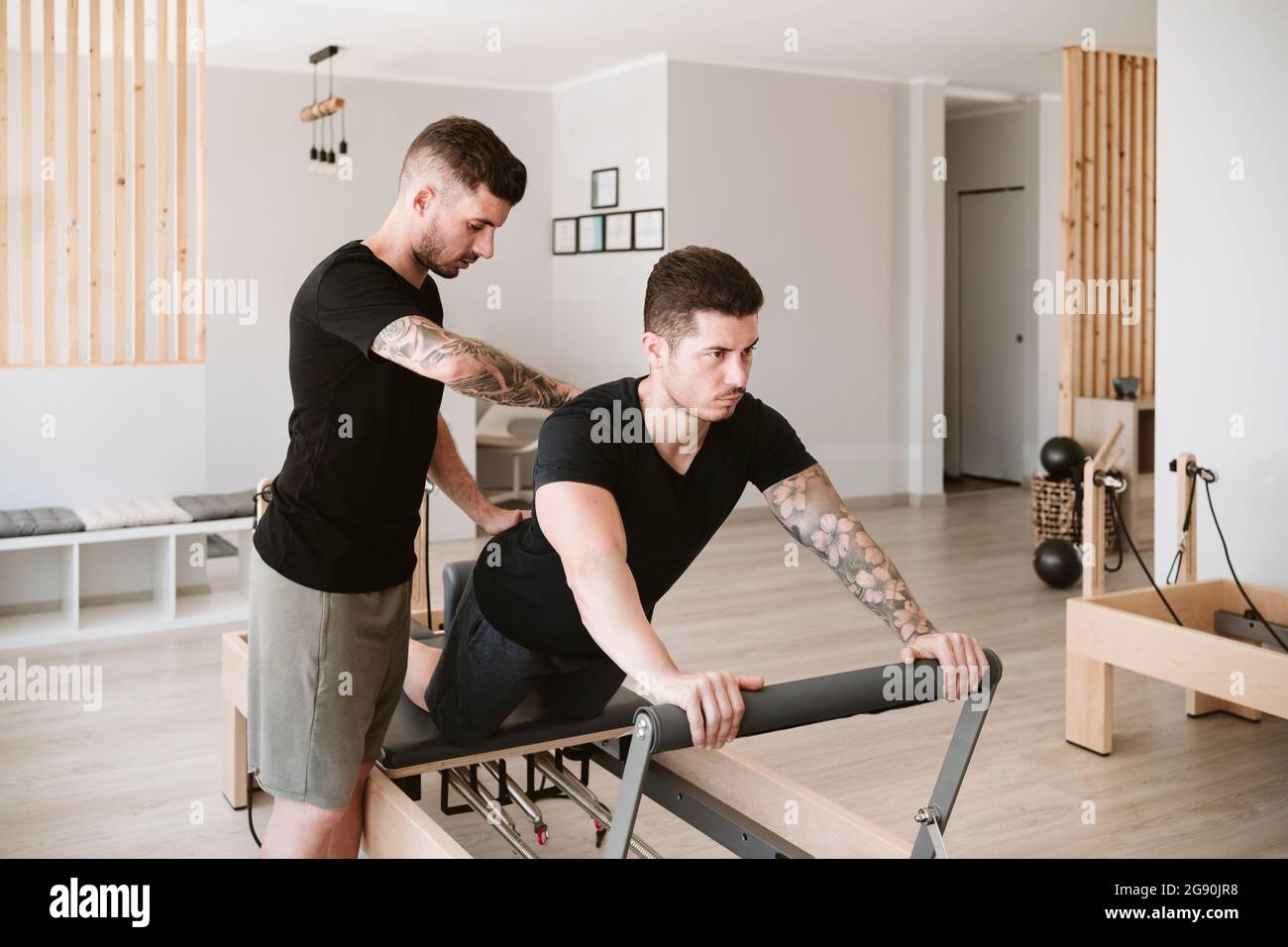 Allenatore di fitness maschile che fornisce supporto mentre l'uomo pratica pilates in studio Foto Stock