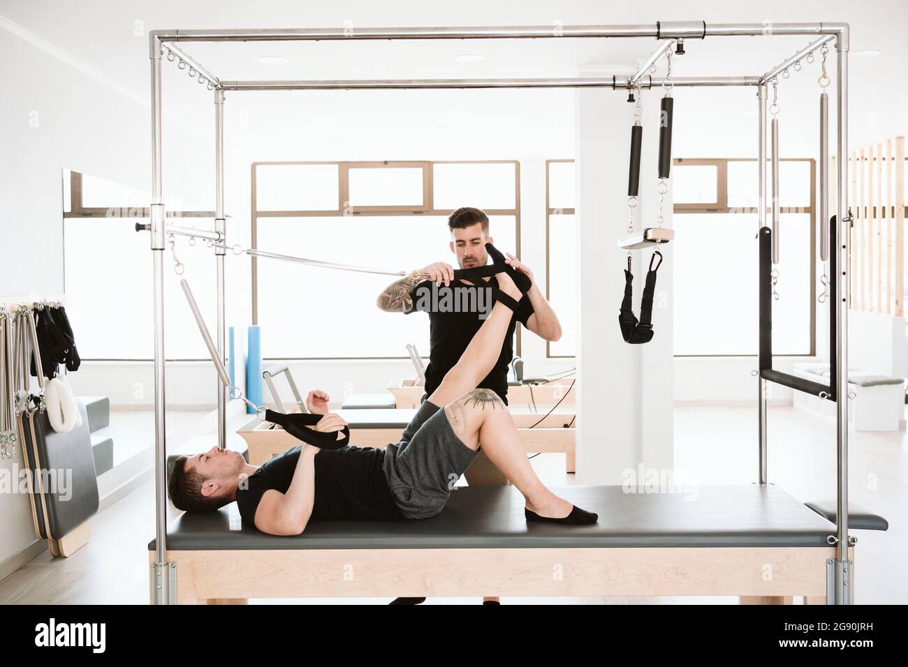 Allenatore di fitness maschile che regola la cinghia mentre l'uomo sdraiato sulla macchina pilates in studio Foto Stock