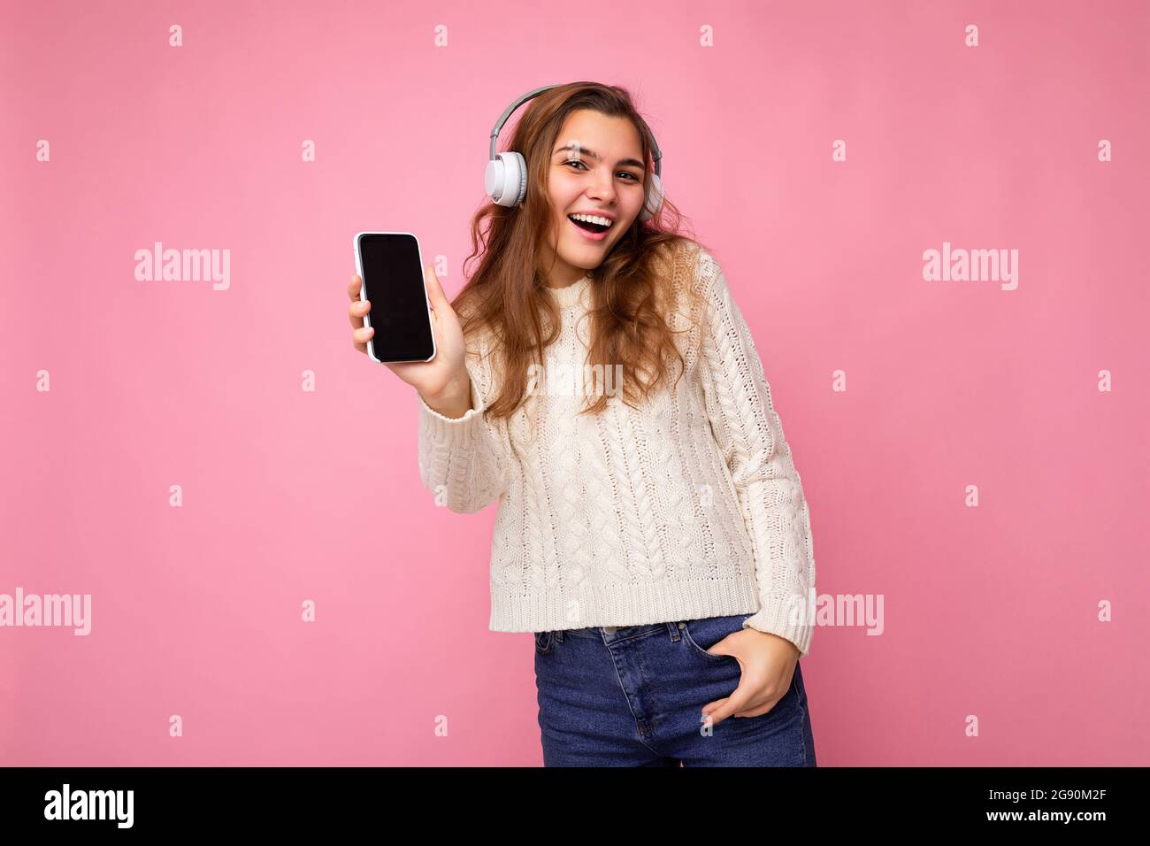 Bella felice sorridente giovane donna indossando elegante abito casual isolato sulla parete di sfondo che tiene e mostra il telefono cellulare con vuoto visualizza per Foto Stock