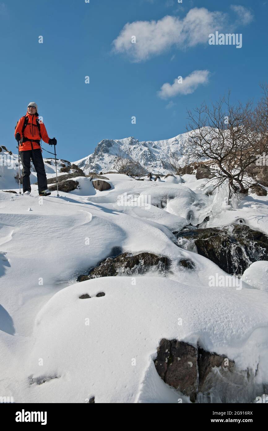 Donna che scende attraverso neve e ghiaccio dal Monte Tryfan Foto Stock
