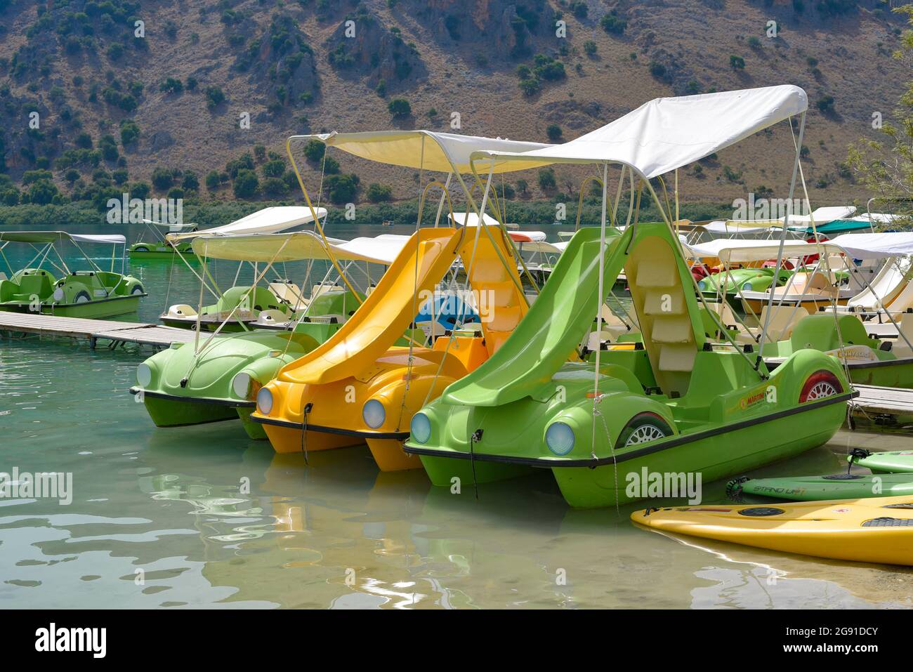 Fila di colorate barche giocattolo per bambini a forma di auto con scivoli  su di loro in un lago intorno alle colline Foto stock - Alamy