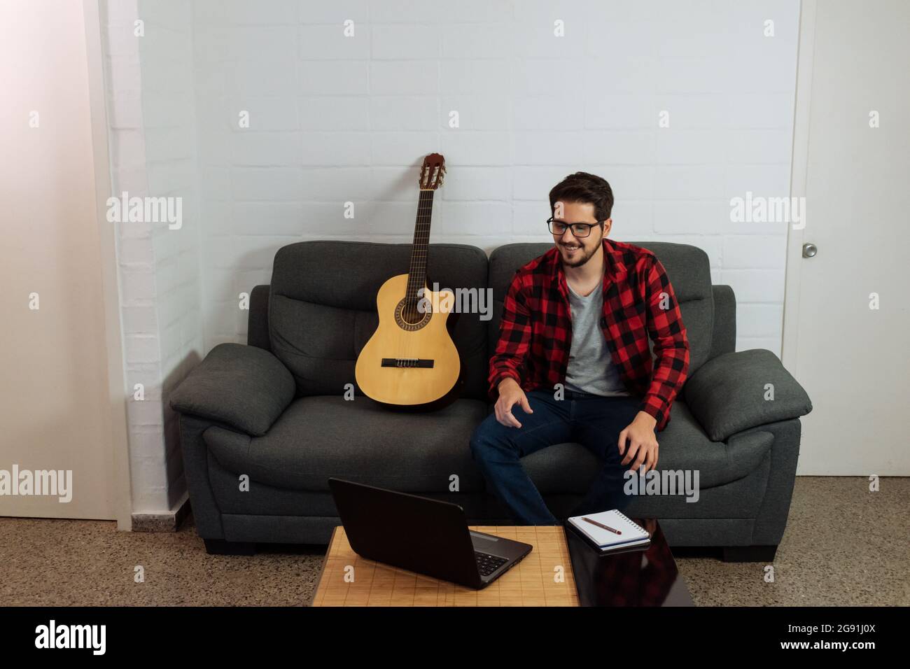 L'uomo latino seduto con la sua chitarra davanti al suo notebook. Foto Stock