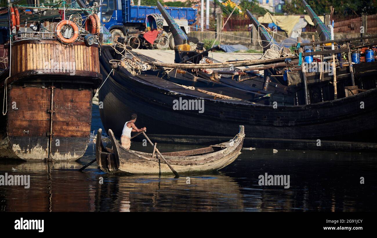 Un pescatore che pedalò tranquillamente lungo i corsi d'acqua del fiume Karnauli e che si affaccia sui grandi pescherecci a strascico Foto Stock