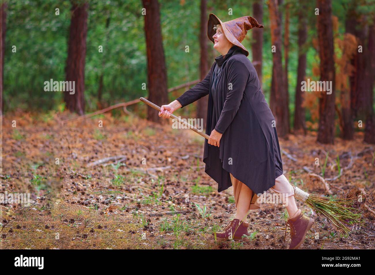 Una strega anziana in un cappello nel bosco, seduta su una scopa, vuole volare Foto Stock