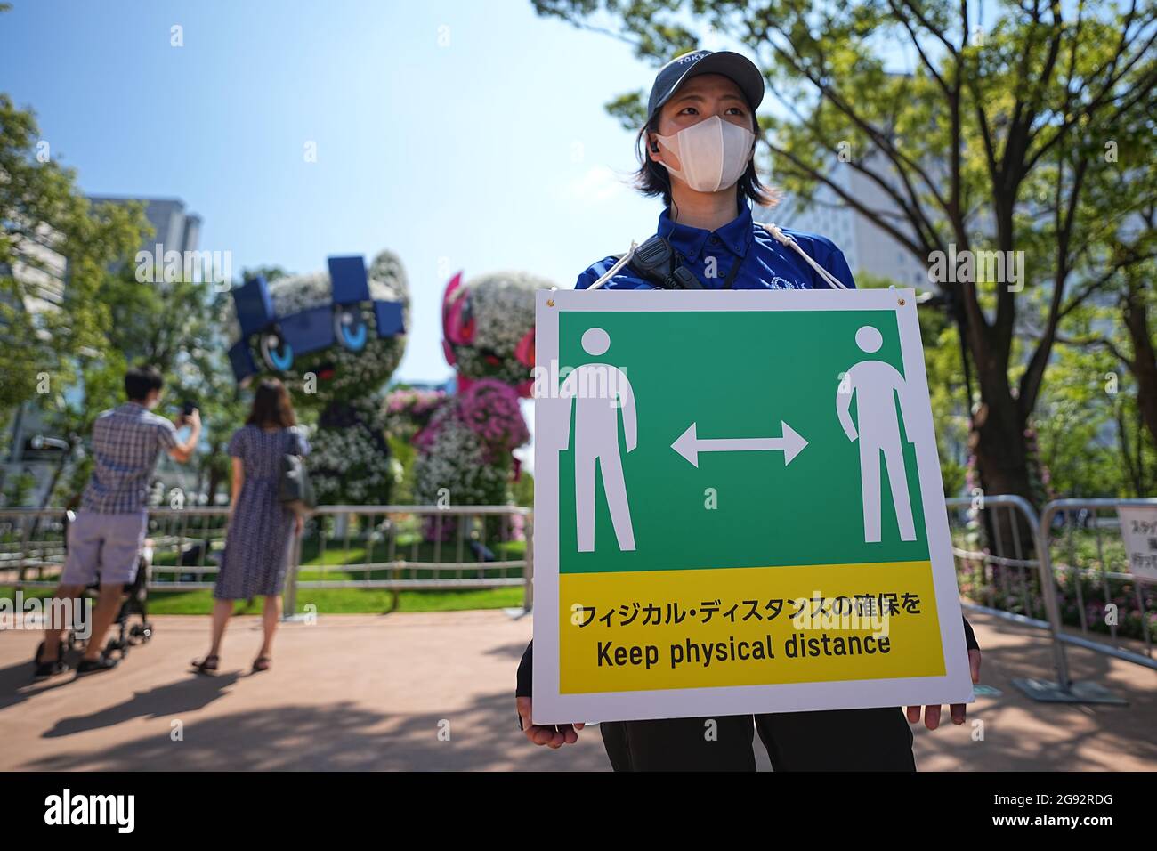 Tokio, Giappone. 24 luglio 2021. I visitatori guardano i personaggi Miraitowa (l), mascotte ufficiale delle Olimpiadi estive di Tokyo 2020, e Someity, mascotte ufficiale delle Paralimpiadi. Un membro dello staff tiene un cartello con un simbolo e le parole 'Keep Physical Distance' per mantenere una distanza sufficiente a proteggere se stessi e gli altri dal contrarre il coronavirus. Le Olimpiadi di Tokyo 2020 si terranno dal 23 luglio 2021 all'8 agosto 2021. Credit: Michael Kappeler/dpa/Alamy Live News Foto Stock