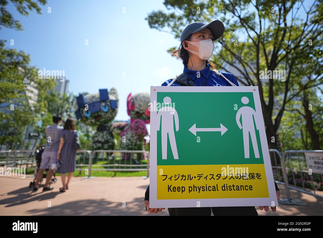 Tokio, Giappone. 24 luglio 2021. I visitatori guardano i personaggi Miraitowa (l), mascotte ufficiale delle Olimpiadi estive di Tokyo 2020, e Someity, mascotte ufficiale delle Paralimpiadi. Un membro dello staff tiene un cartello con un simbolo e le parole 'Keep Physical Distance' per mantenere una distanza sufficiente a proteggere se stessi e gli altri dal contrarre il coronavirus. Le Olimpiadi di Tokyo 2020 si terranno dal 23 luglio 2021 all'8 agosto 2021. Credit: Michael Kappeler/dpa/Alamy Live News Foto Stock