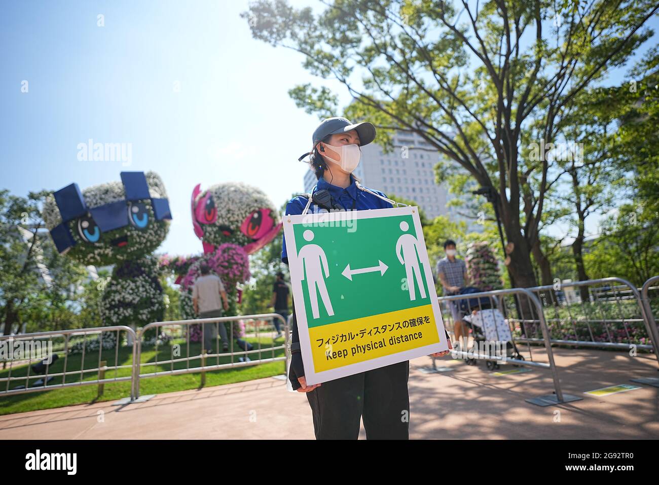 Tokio, Giappone. 24 luglio 2021. I visitatori guardano i personaggi Miraitowa (l), mascotte ufficiale delle Olimpiadi estive di Tokyo 2020, e Someity, mascotte ufficiale delle Paralimpiadi. Un membro dello staff tiene un cartello con un simbolo e le parole 'Keep Physical Distance' per mantenere una distanza sufficiente a proteggere se stessi e gli altri dal contrarre il coronavirus. Le Olimpiadi di Tokyo 2020 si terranno dal 23 luglio 2021 all'8 agosto 2021. Credit: Michael Kappeler/dpa/Alamy Live News Foto Stock