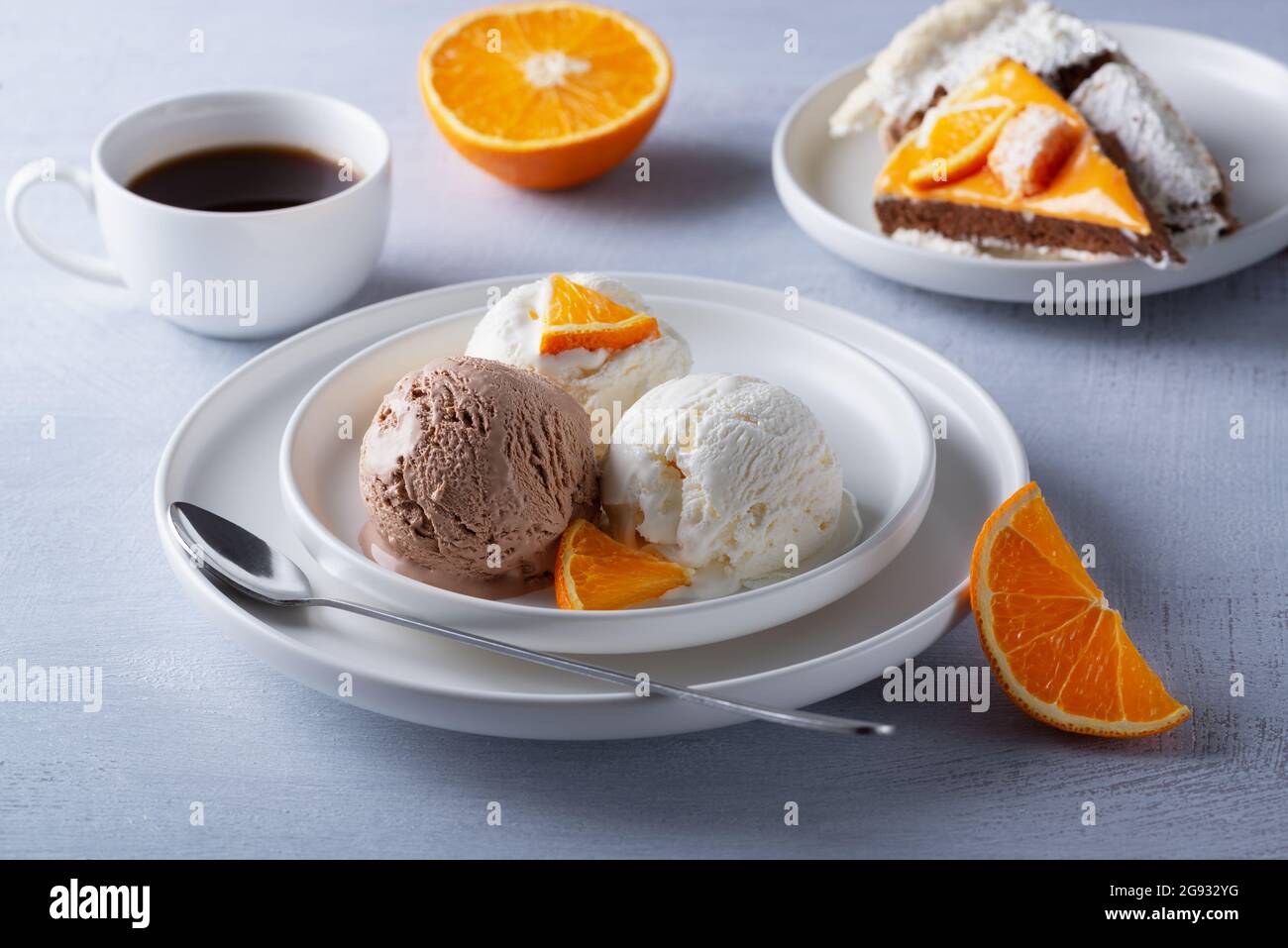Gelato alla vaniglia e al cioccolato, torta e fette d'arancia su un tavolo di legno chiaro Foto Stock