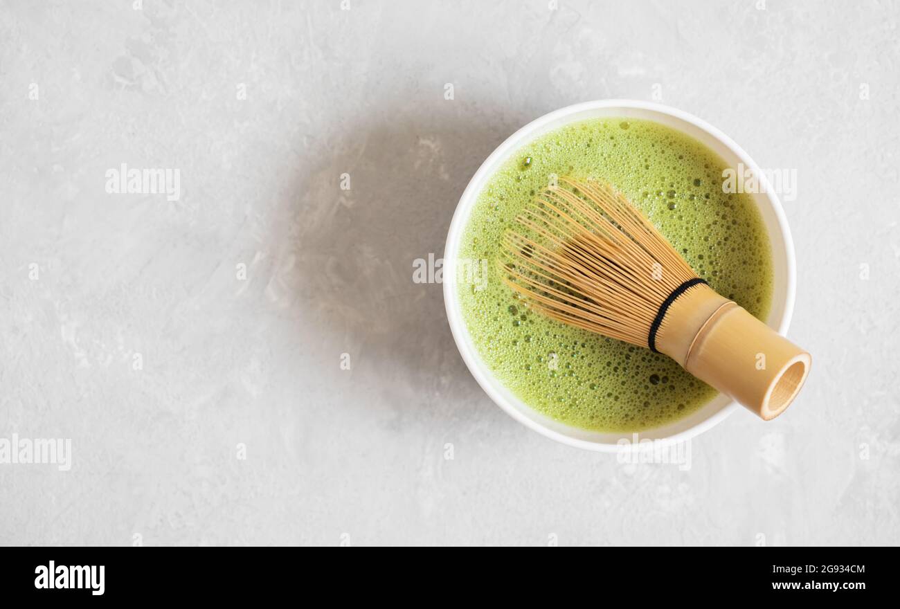 Tè Matcha e un bambu frusta su uno sfondo grigio di cemento. Cucina tè verde matcha. Bevanda tradizionale giapponese. Spazio di copia, vista dall'alto, disposizione piatta. Foto Stock