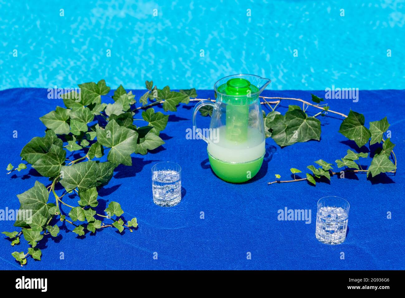 Un telo da spiaggia blu a bordo piscina viene utilizzato come tovaglia con due bicchieri di ghiaccio e acqua frizzante e una caraffa di succo di pompelmo Foto Stock