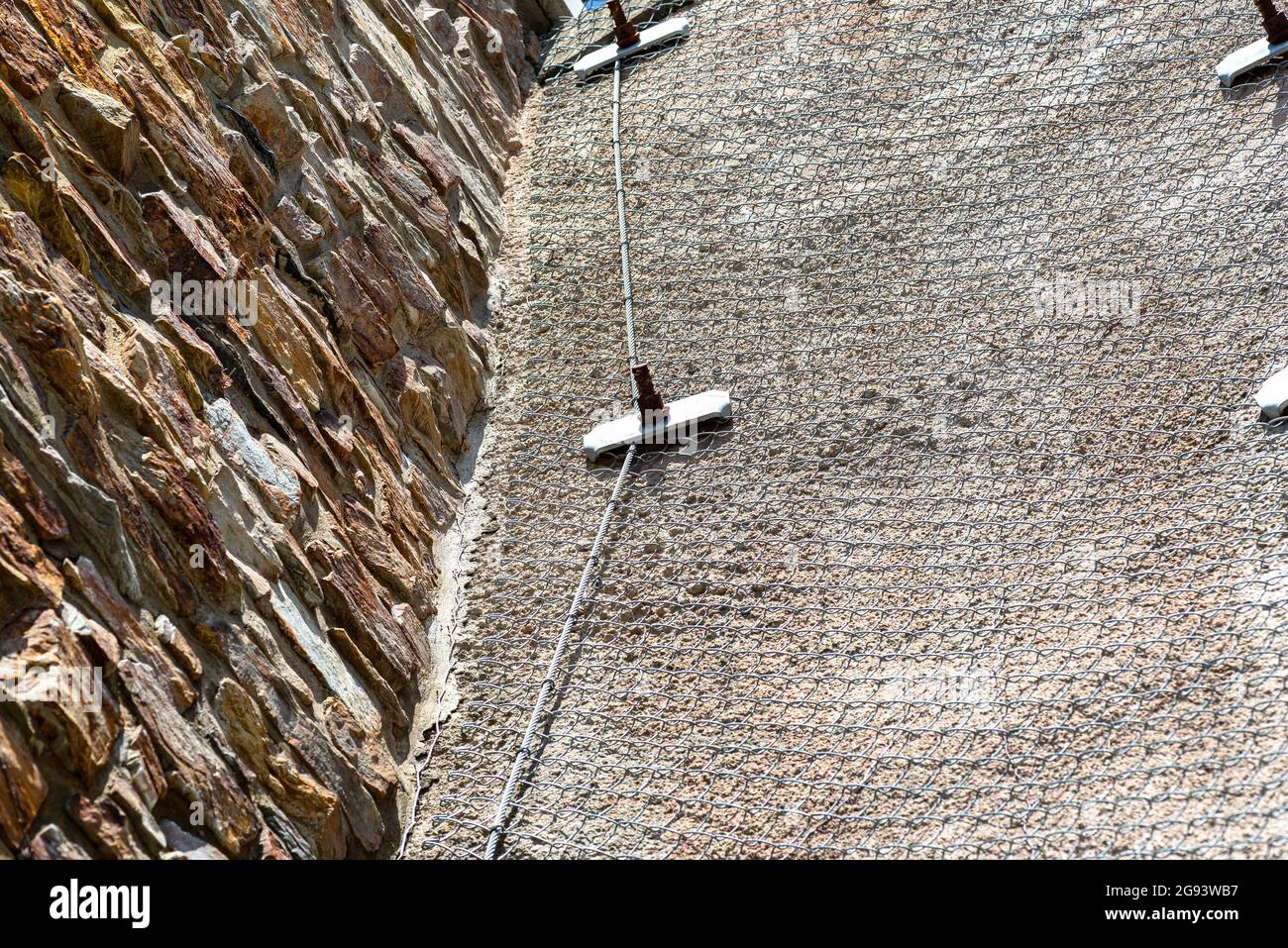 Una parete di pietra in piedi da una strada fissata con una rete metallica zincata, fuoco selettivo. Foto Stock